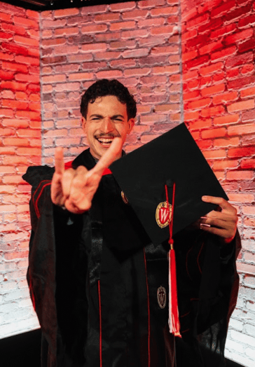 Jacob Wanger is an up-and-coming stand-up comedian and writer who graduated this May from the University of Wisconsin-Madison with Bachelor of Arts in both Philosophy and Communication Arts. Like many Philosophy majors before him, he is currently unemployed. Before landing on comedy, Jacob found himself in a wide-array of jobs such as being a Personal Fitness Trainer, Stock Analyst, and made for damn fine DoorDash driver (4.98⭐). Immediately after graduation, Mr. Wanger made the incredibly responsible decision to pursue comedy full time. His method of entry into America’s lowest form of show-business, embarking on the uniquely American odyssey of the cross-country road trip, doing so from the complicated comforts of a camper van. Over the course of the next year (or whenever his savings runs out), Jacob will be travelling the country in search of meaning, connection, and stage time. Along the way, he will be writing screenplays and chipping away at his first novel. In his young career, Jacob has already performed in cities such as Madison, Chicago, Phoenix, New York, and Barcelona, picking up several private bookings along the way. When he’s not on stage, you can usually find him doing literally anything. This dude cannot sit still for the life of him. Luckily, this inability for stability gives life plenty of opportunity to write jokes for him. His comedy leans into storytelling, absurdity, and making sense of the deeper complexities of life through the eyes of a goofy 22-year-old.